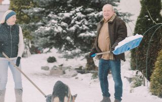 Retired Couple Shoveling Snow With Dog
